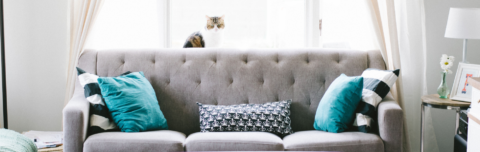 A clean gray couch with blue cushions in front of a window with drapes
